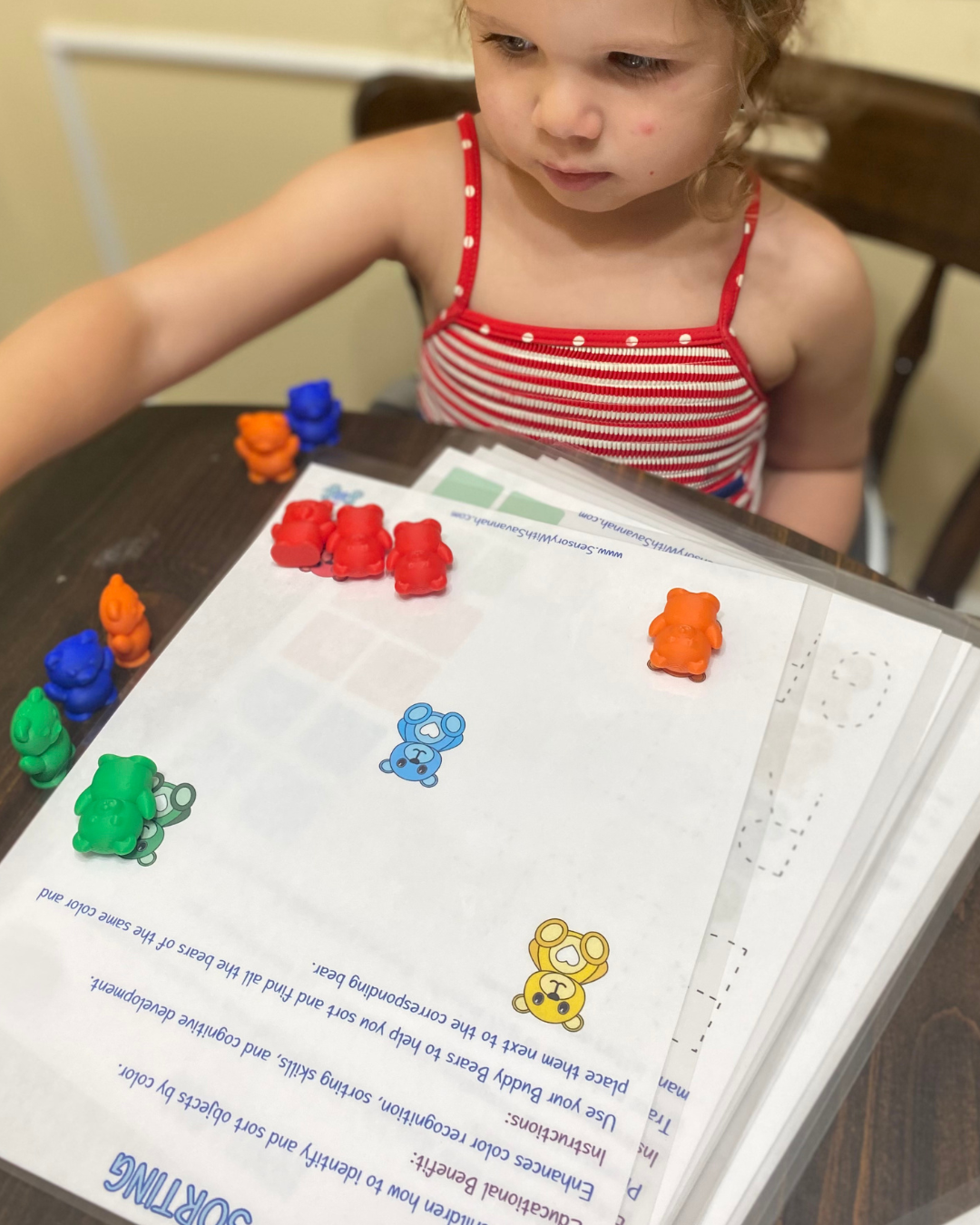 Toddler sorting Buddy Bears by color on activity sheet to enhance color recognition and sorting skills.