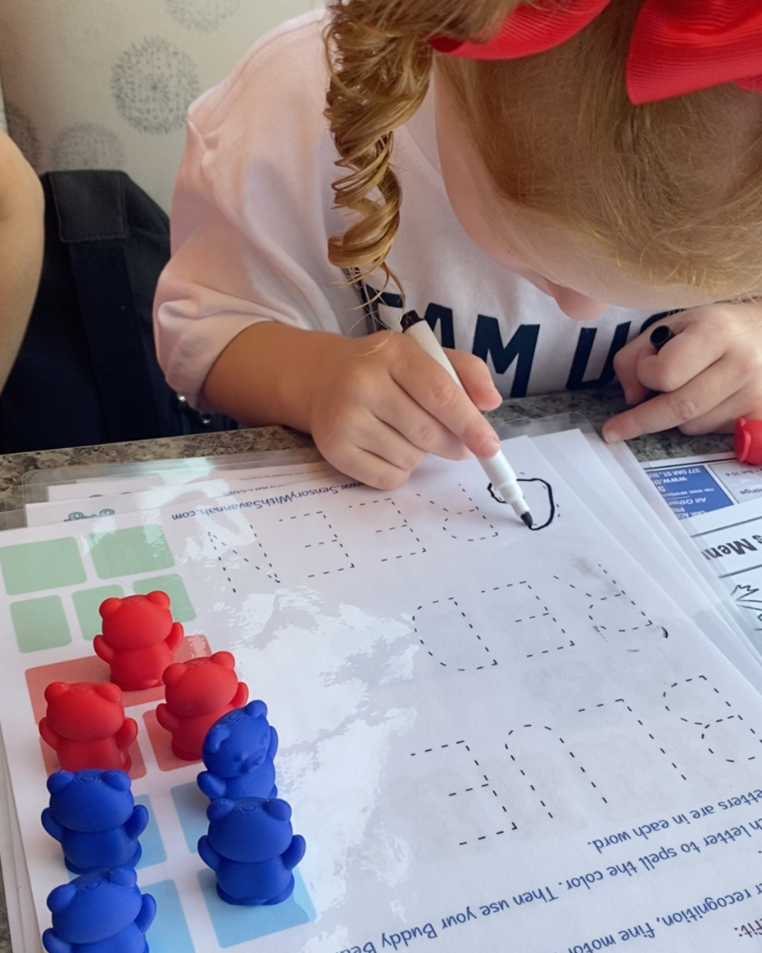 Toddler tracing words with Buddy Bears activity sheets and dry erase marker for early literacy skills.