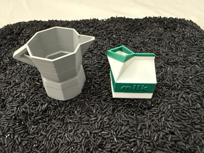 May include: A gray, geometric coffee maker and a white milk carton with green accents and the word "milk" printed on it. The objects are set against a backdrop of black rice.