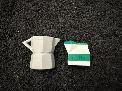 May include: A gray, geometric coffee maker and a white and green milk carton are displayed on a bed of black rice. The milk carton has the word "milk" printed on it. The objects are likely decorative.