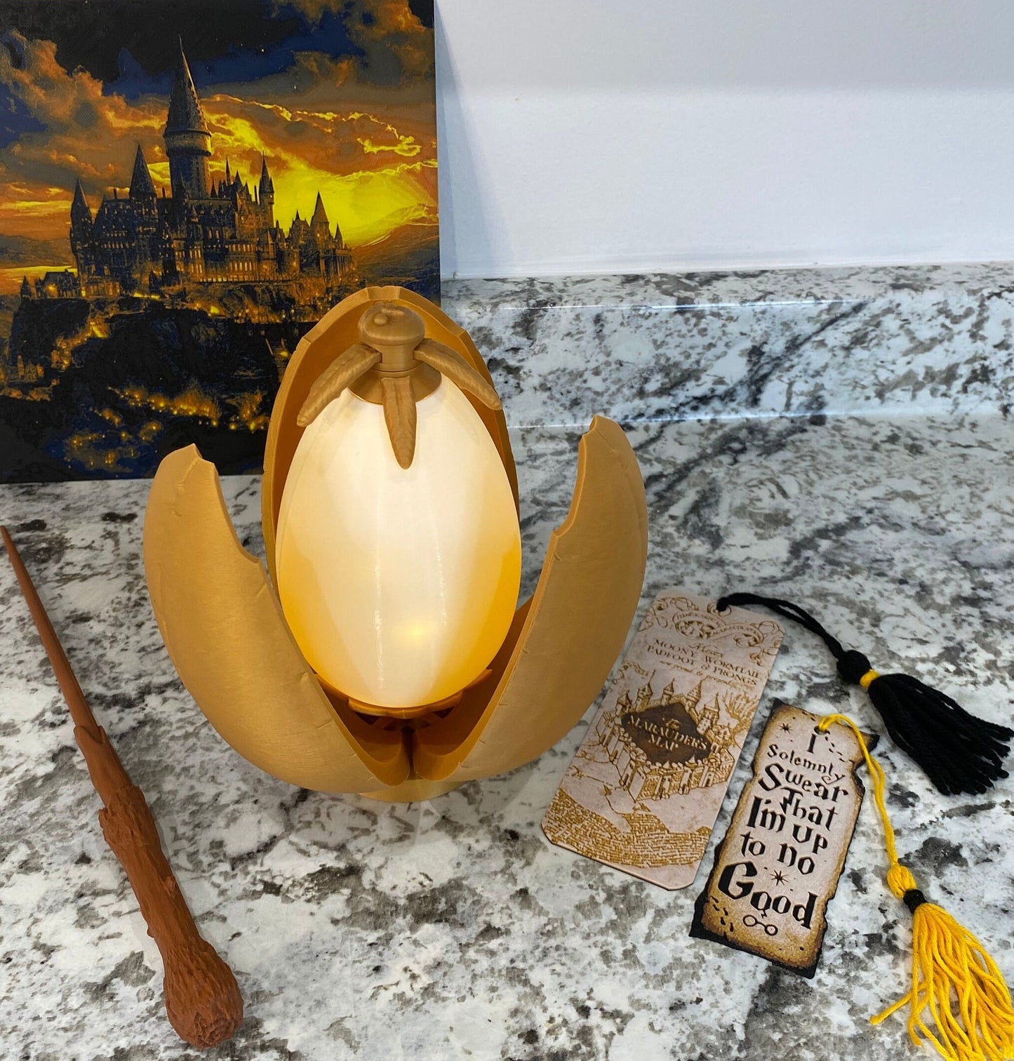 May include: A golden egg-shaped container with a glowing white interior, a brown wand, and a bookmark with the text "I solemnly swear that I'm up to no good" and a map of Hogwarts.