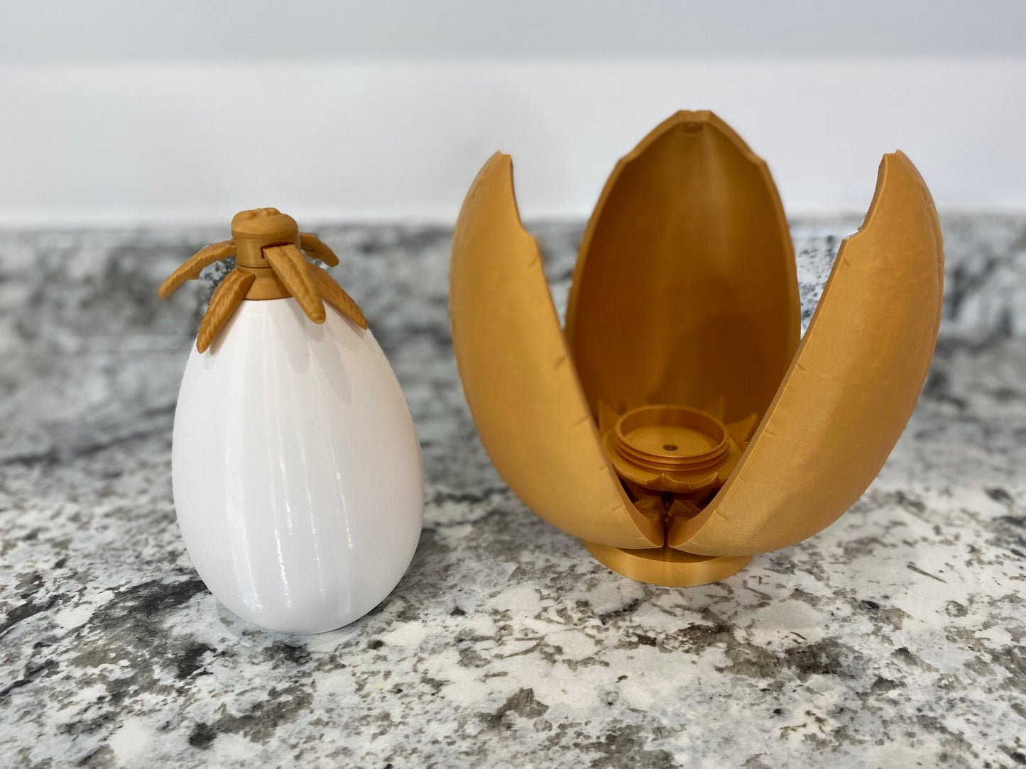 May include: A white egg-shaped container with a gold top and a gold egg-shaped container that is open and has three sections.