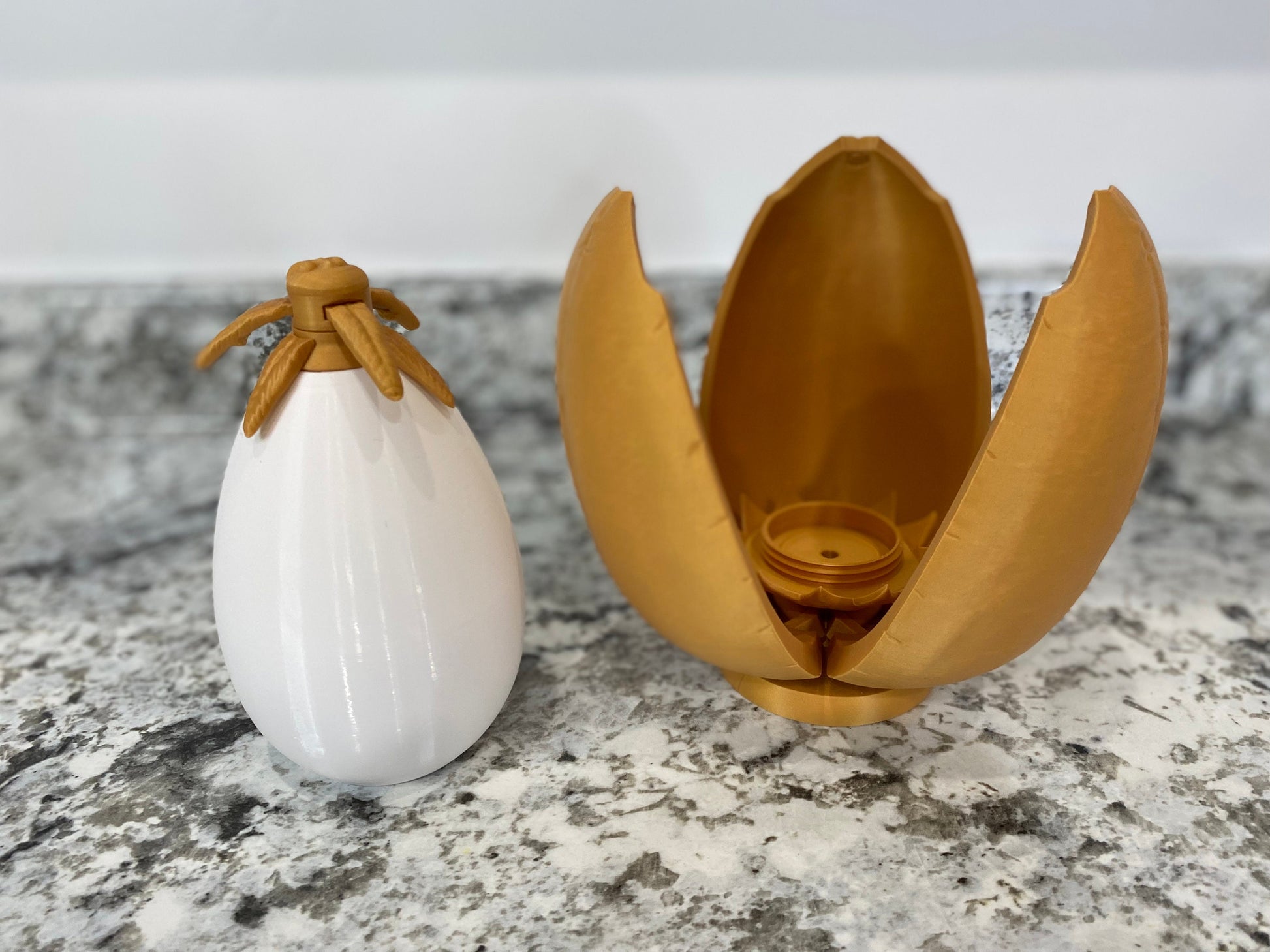 May include: A white egg-shaped container with a gold top and a gold egg-shaped container that is open and has three sections.