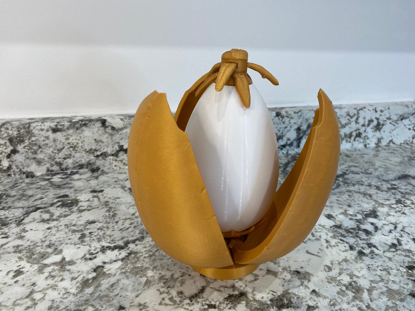 May include: A gold-colored plastic egg with a white egg inside. The egg is open and the white egg is visible. The egg is a toy.