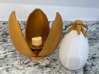 May include: A gold egg-shaped container with a candle inside, and a white egg-shaped container with a gold top.
