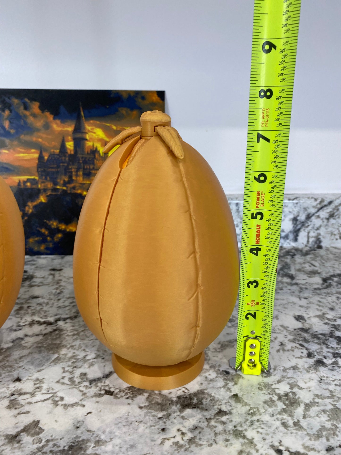 May include: Two gold-colored ceramic eggs with a textured surface. The egg on the right is 7 inches tall and has a small opening at the top.