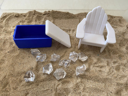 May include: A blue cooler with a white lid, a white plastic beach chair, and clear ice cubes on a sandy surface.