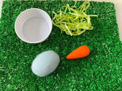 May include: A white wicker basket, a light blue egg, an orange carrot, and green shredded paper on a bed of green rice.