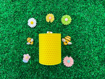 May include: A yellow honeycomb-shaped container surrounded by plastic bees and flowers on a green surface.