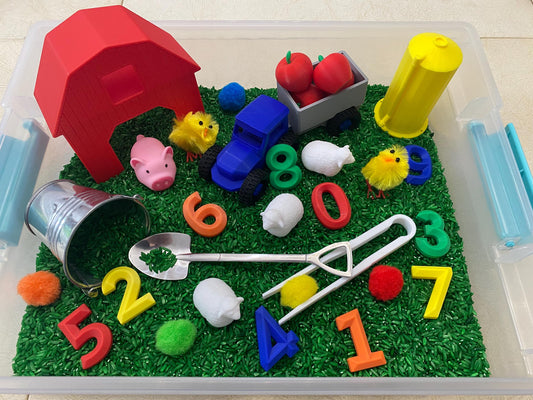 May include: A red barn, a blue toy truck, a bucket, a shovel, and a variety of farm animals are placed in a clear plastic bin filled with green rice. The numbers 1 through 8 are scattered throughout the bin.