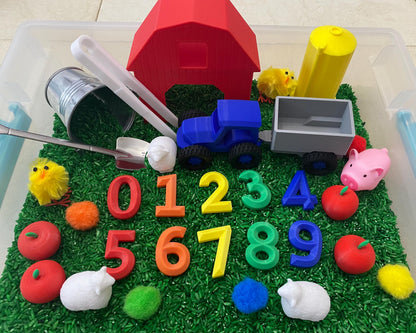 May include: A red barn, a blue tractor with a gray wagon, a yellow silo, and a set of colorful numbers 0-9 are in a sensory bin filled with green rice. There are also red apples, white lambs, and yellow chicks.