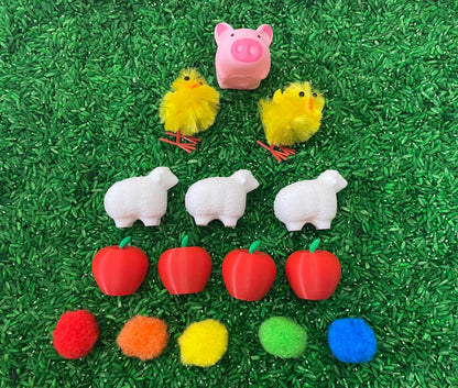 May include: A farm-themed sensory bin with a pink pig, yellow chicks, white sheep, red apples, and colorful pom-poms.