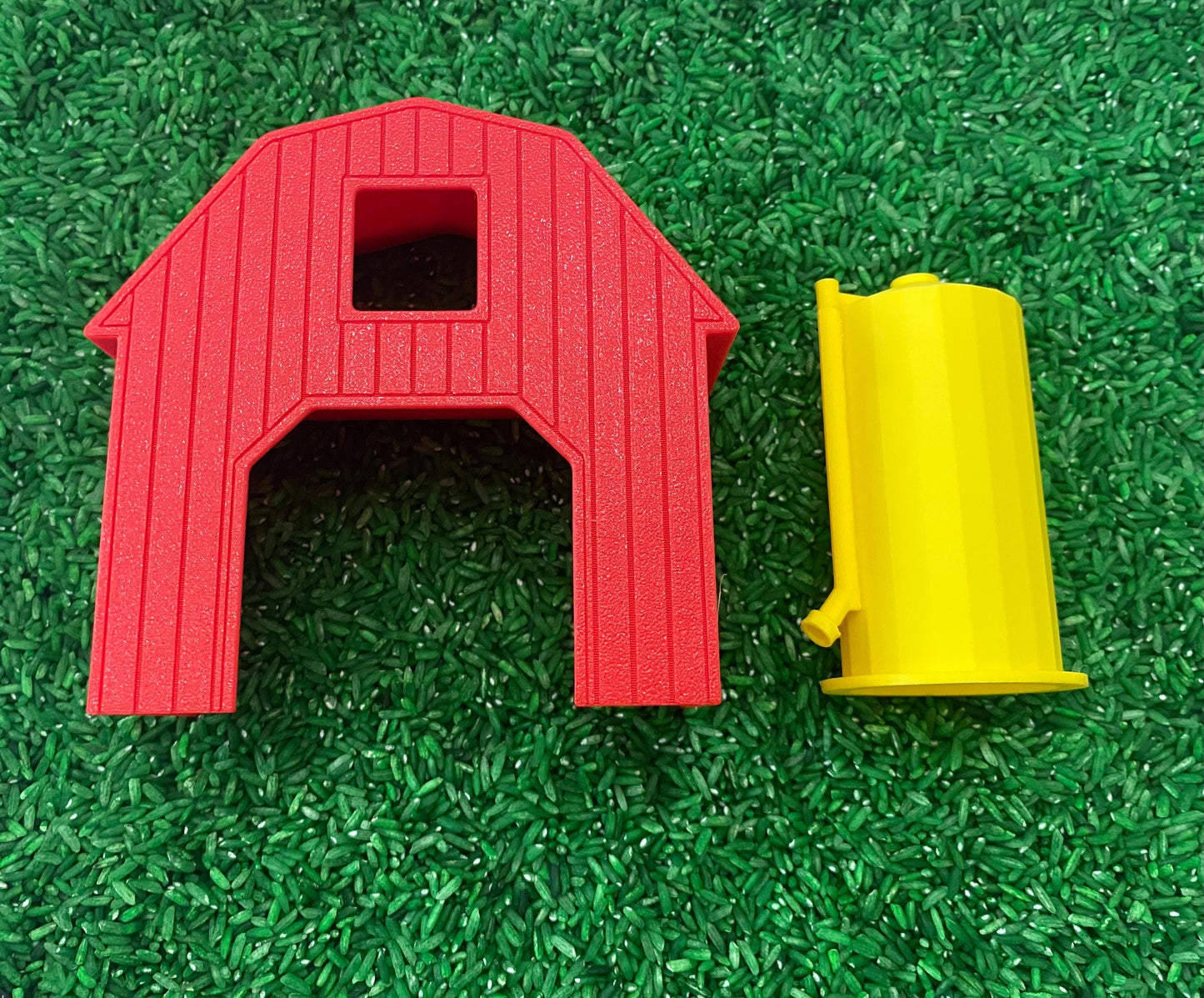 May include: A red plastic barn with a yellow silo. The barn has a door and a window. The silo is tall and cylindrical.