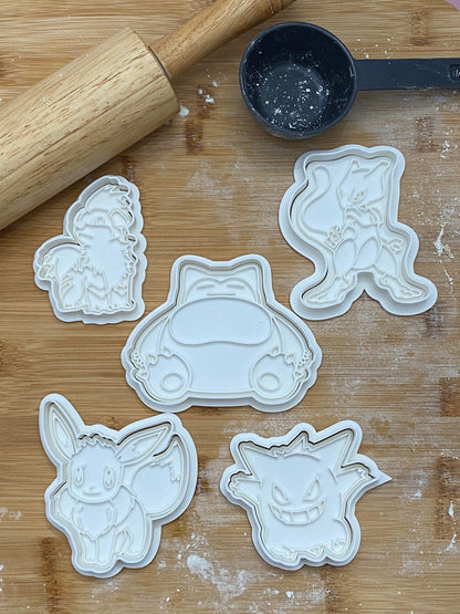 May include: Five white plastic cookie cutters shaped like Pokemon characters. The characters are Eevee, Snorlax, Mewtwo, Gengar, and a Eevee evolution.