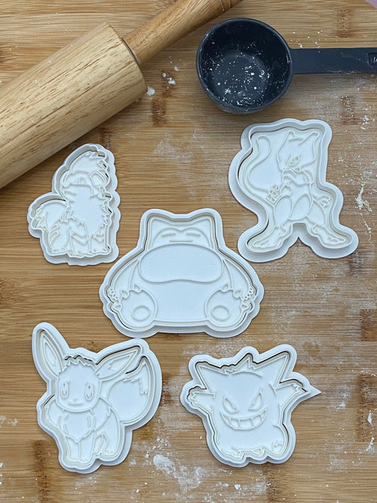 May include: Five white plastic cookie cutters shaped like Pokemon characters. The characters are Eevee, Snorlax, Mewtwo, Gengar, and a Eevee evolution.