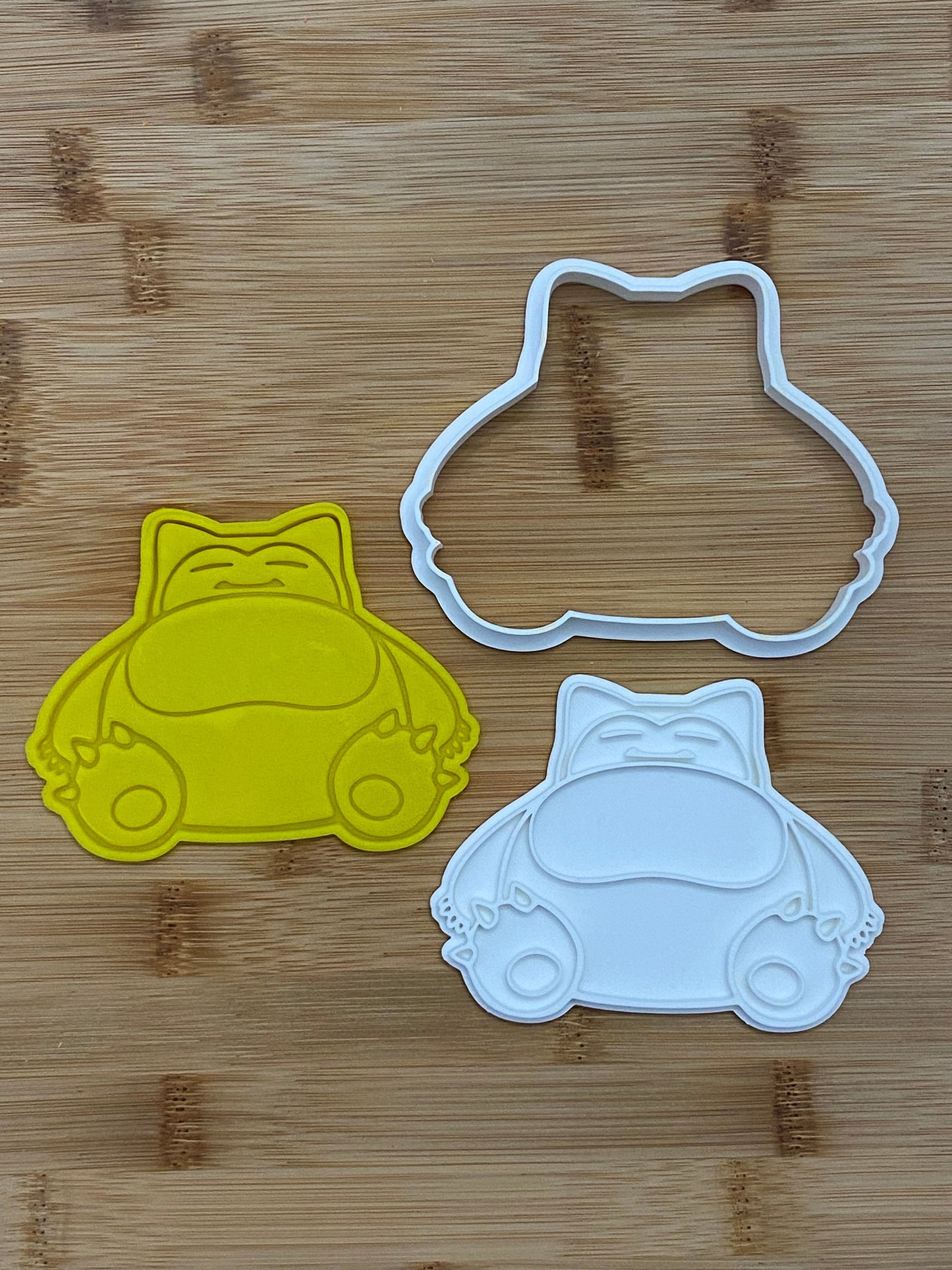 May include: Two cookie cutters, one yellow and one white, shaped like a cartoon character with a round body, short legs, and a sleepy expression.