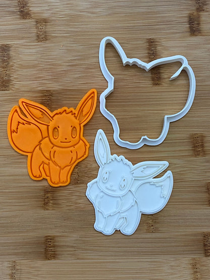 May include: Two cookie cutters, one orange and one white, shaped like a cartoon Eevee Pokemon.