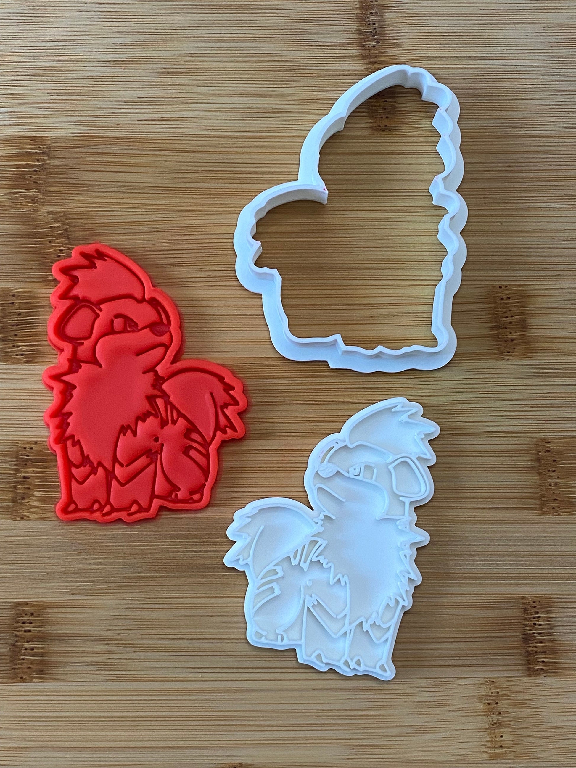 May include: Two cookie cutters, one red and one white, shaped like a cartoon dog with fluffy fur.