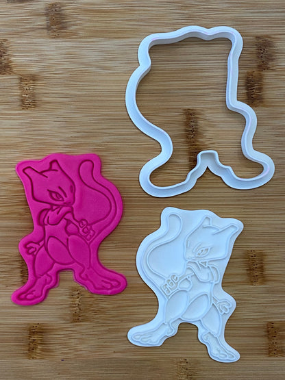 May include: Two cookie cutters, one pink and one white, shaped like a Pokemon character. The character is standing with its arms crossed and has a tail.
