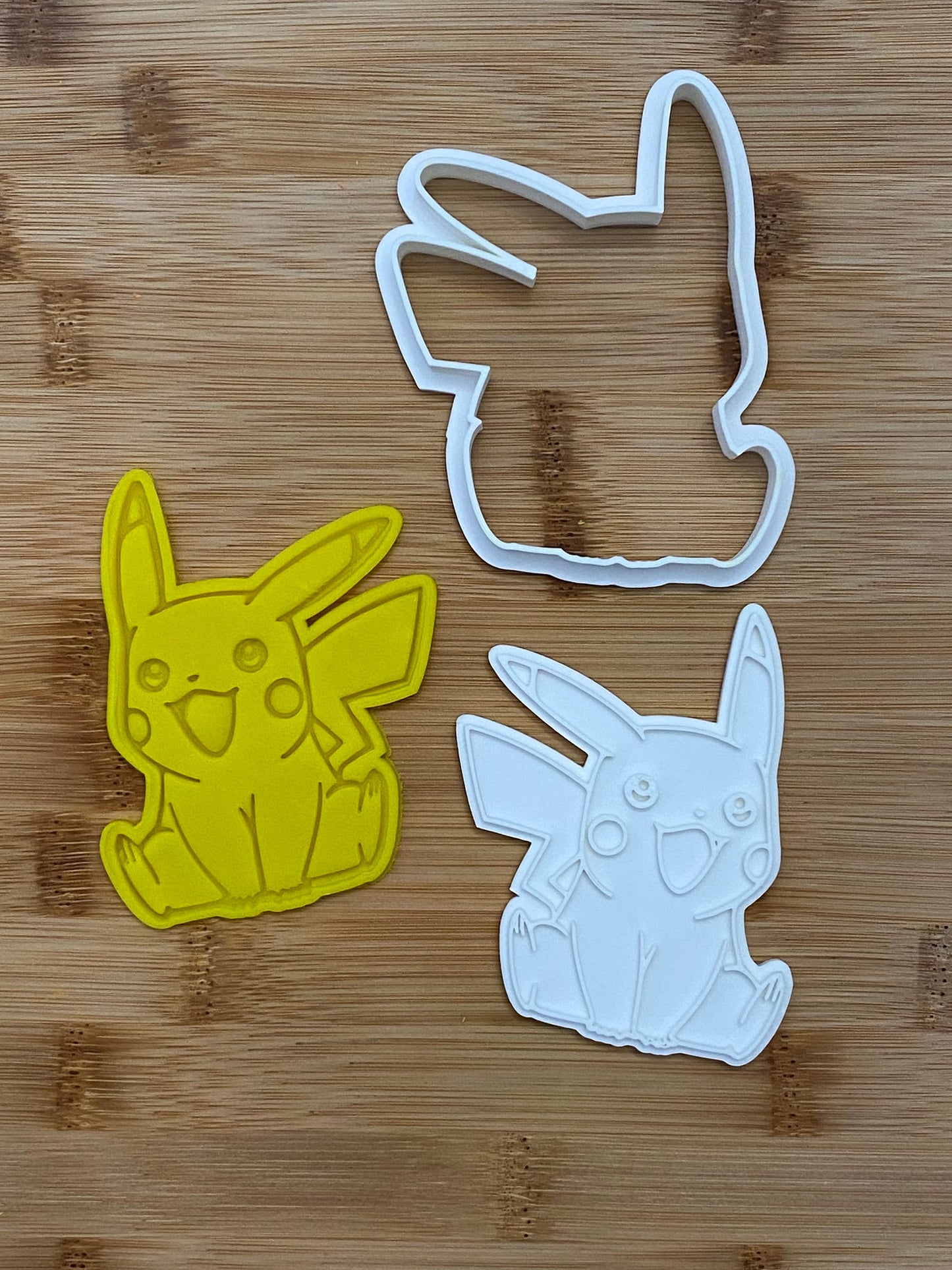 May include: Two cookie cutters, one yellow and one white, shaped like Pikachu, a popular cartoon character.
