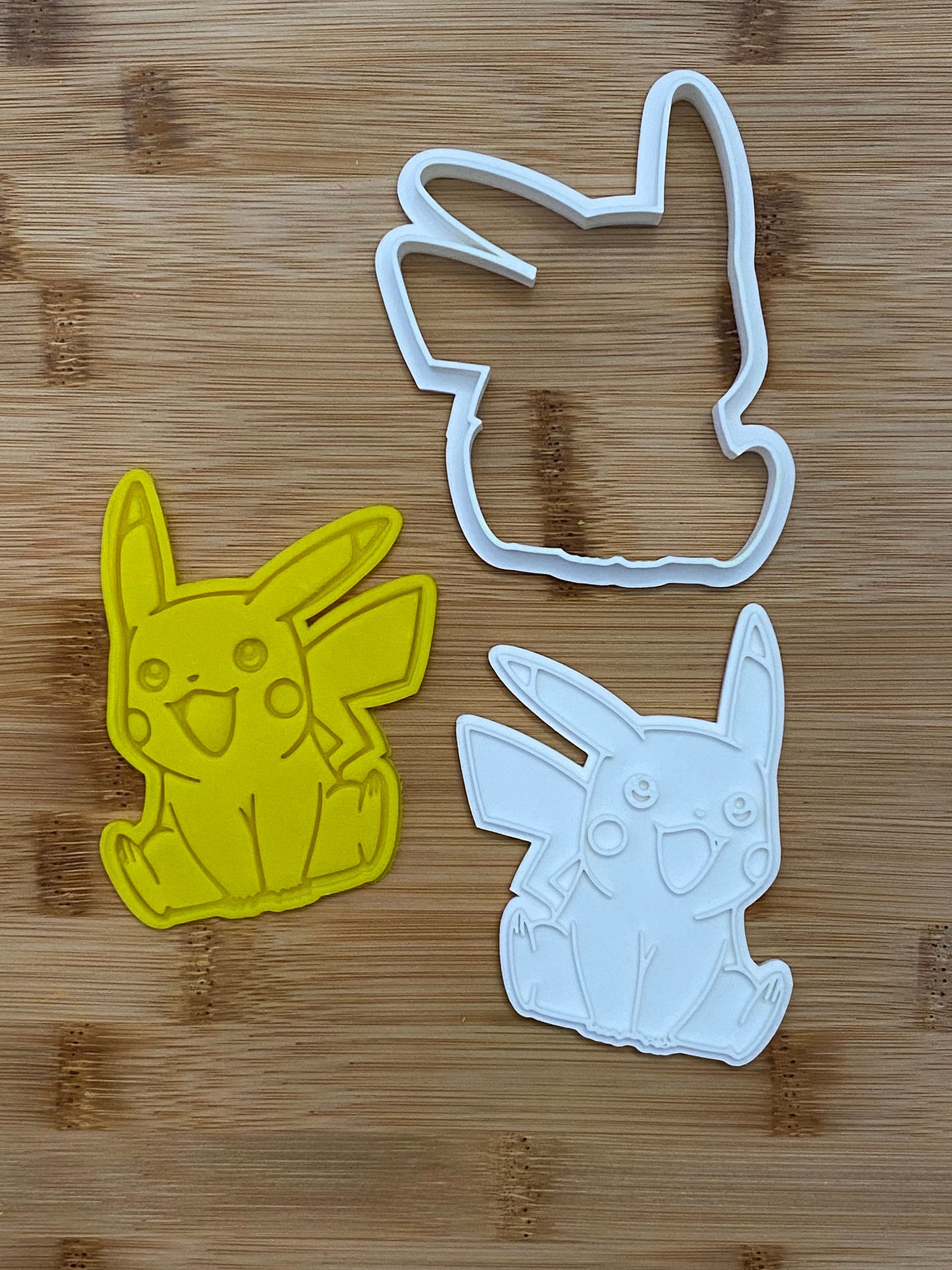 May include: Two cookie cutters, one yellow and one white, shaped like Pikachu, a popular cartoon character.