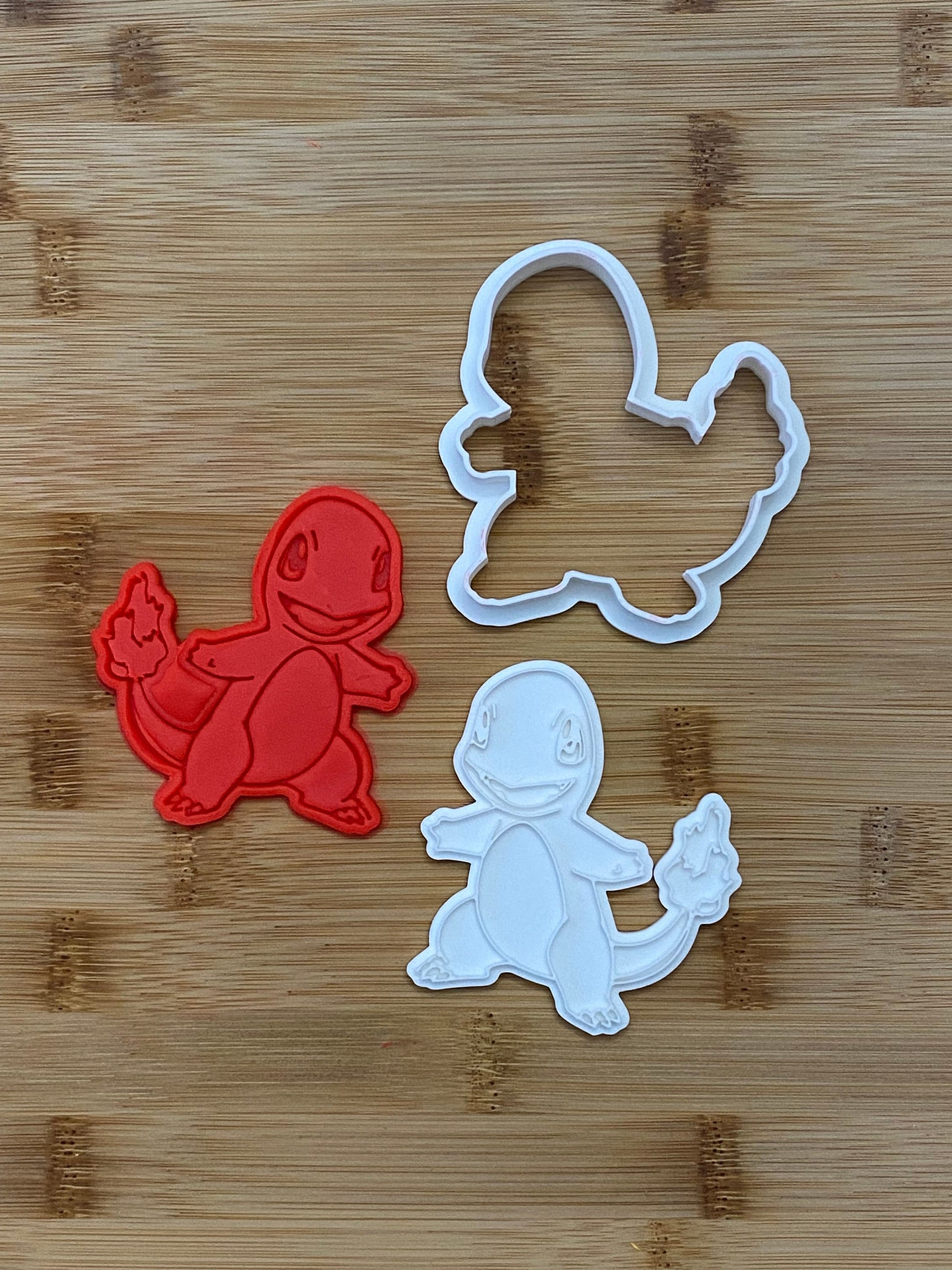 May include: Two cookie cutters, one red and one white, shaped like a cartoon character with a tail and a flame.