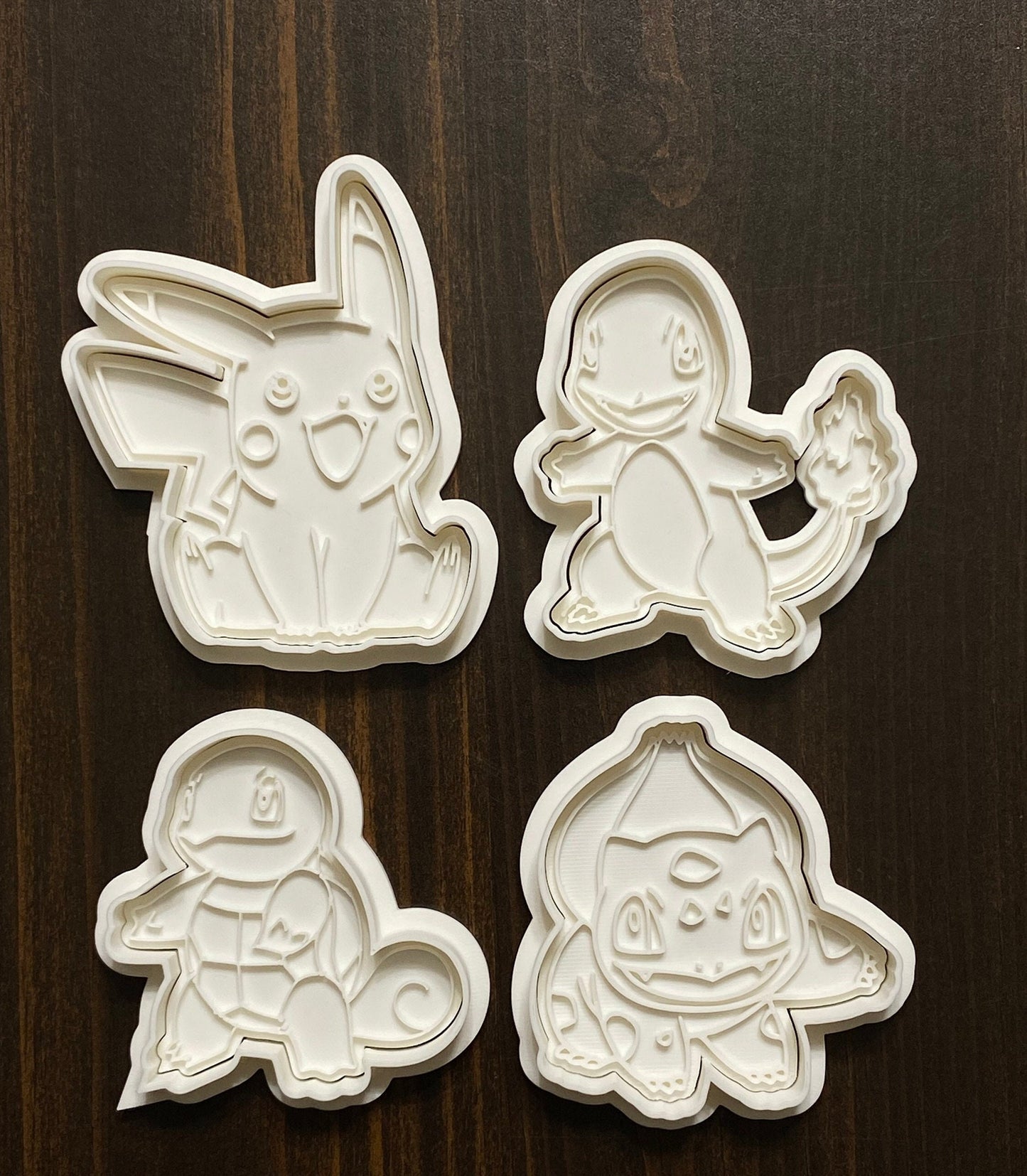 May include: Four white plastic cookie cutters shaped like Pokemon characters: Pikachu, Charmander, Squirtle, and Charmeleon.