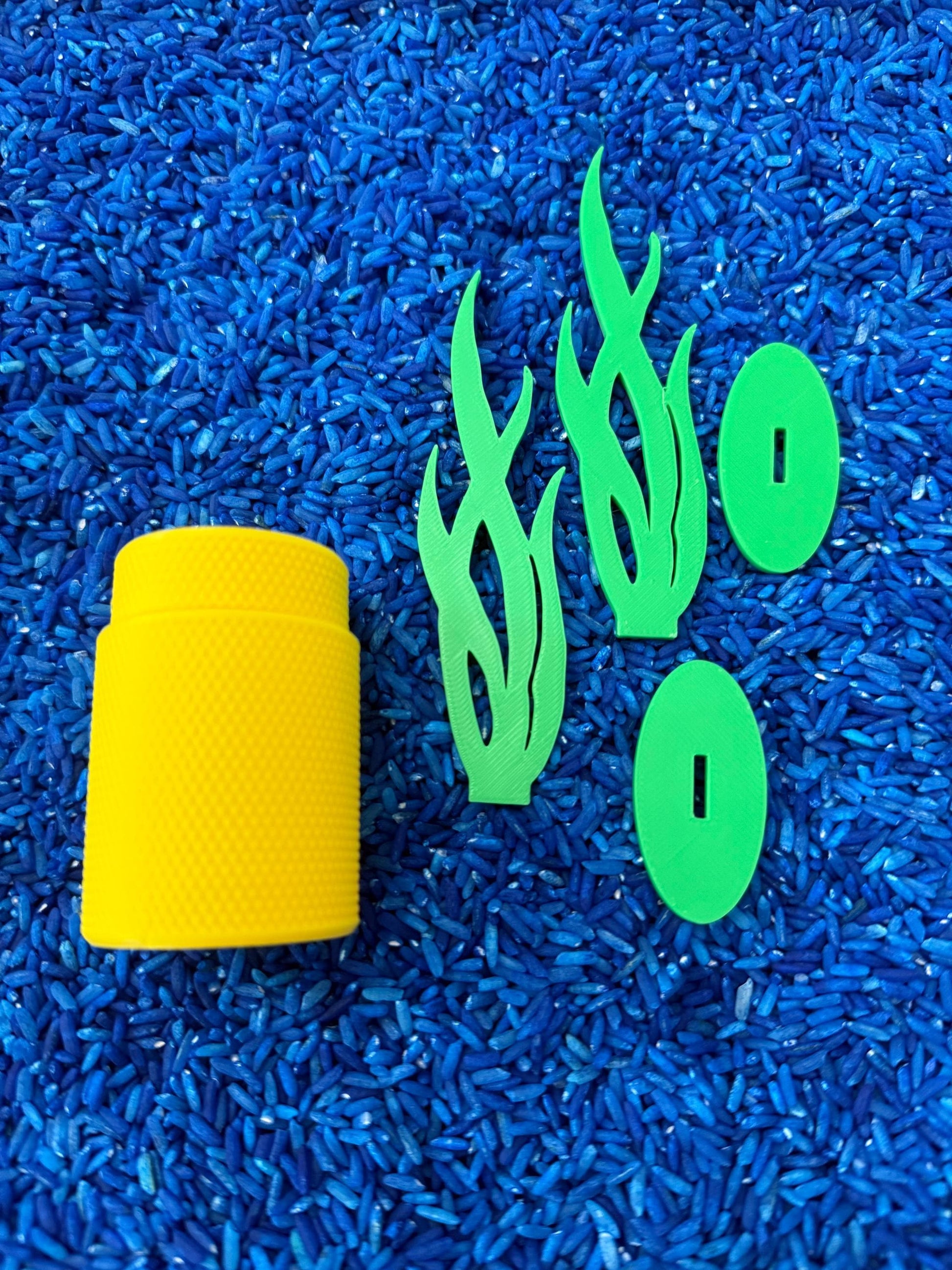 May include: A yellow cylinder with a textured surface, two green flame-shaped pieces, and two green oval-shaped pieces on a blue background.